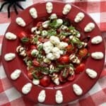 Red bowl with Halloween caprese salad and mozzarella skulls spaced around the flat rim of the bowl.