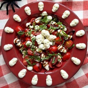 Red bowl with Halloween caprese salad and mozzarella skulls spaced around the flat rim of the bowl.