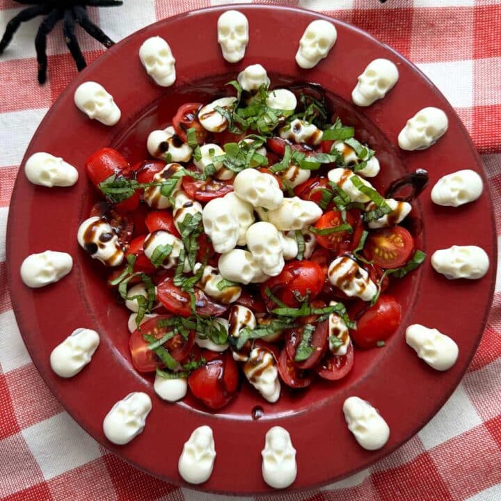Red bowl with Halloween caprese salad and mozzarella skulls spaced around the flat rim of the bowl.