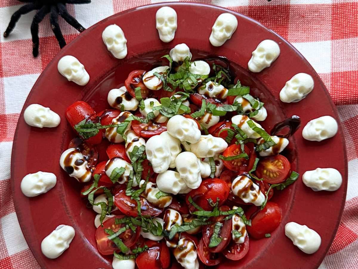 Red bowl with Halloween Caprese Salad with mozzarella skulls arranged around the flat rim.