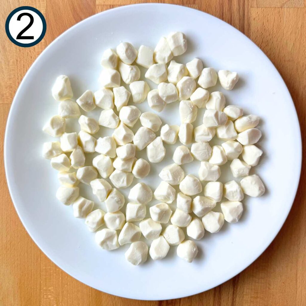 Fresh mozzarella pearls spread out on a white plate.