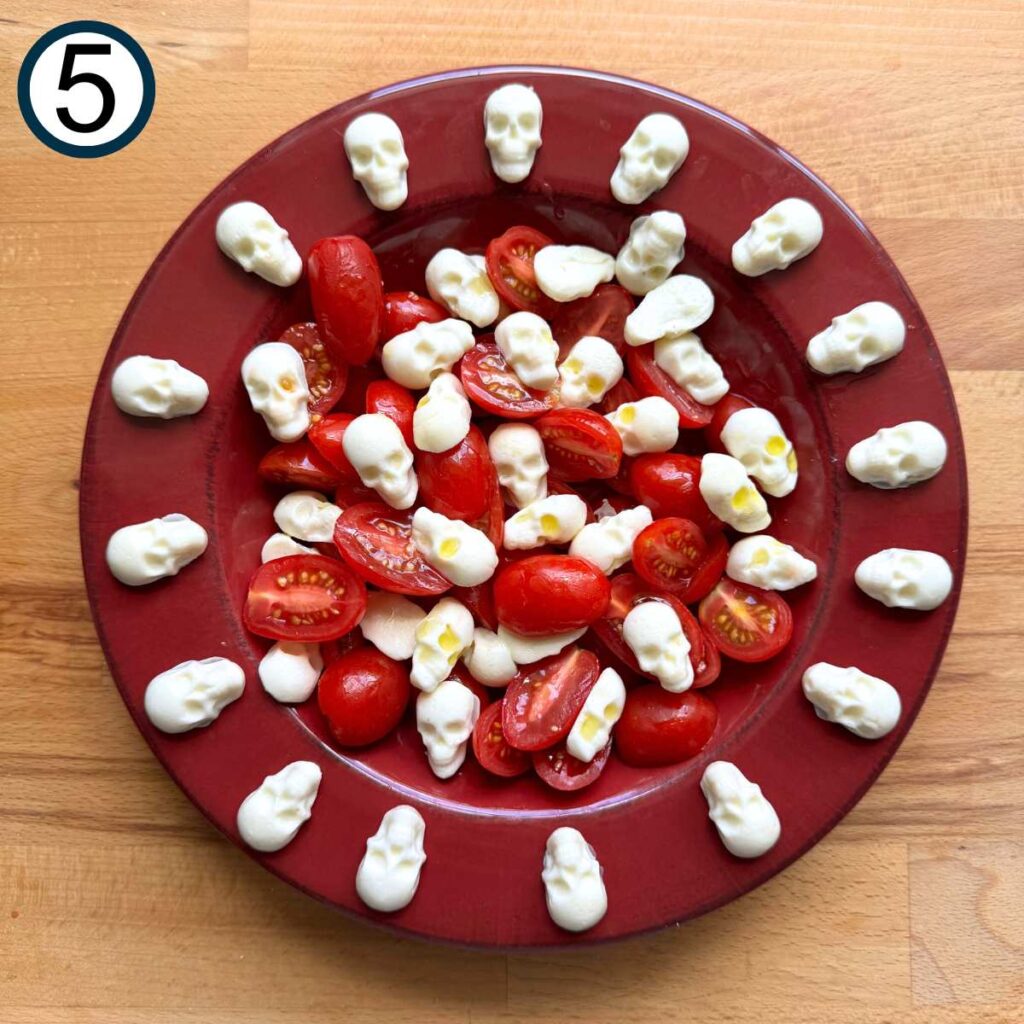 Red plate with mozzarella skulls and grape tomatoes that have been sliced in half.