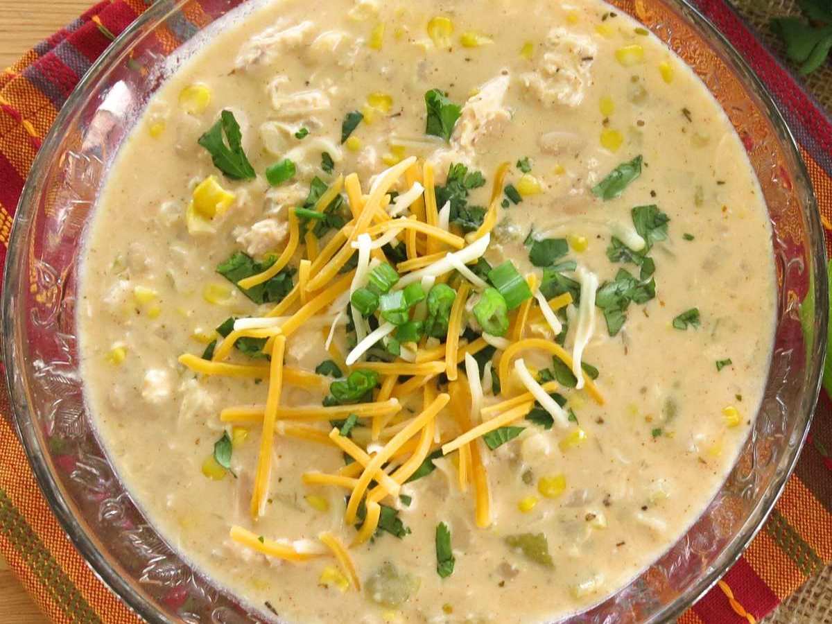 Glass bowl with creamy white bean chicken chili topped with green onions and shreds of cheese.