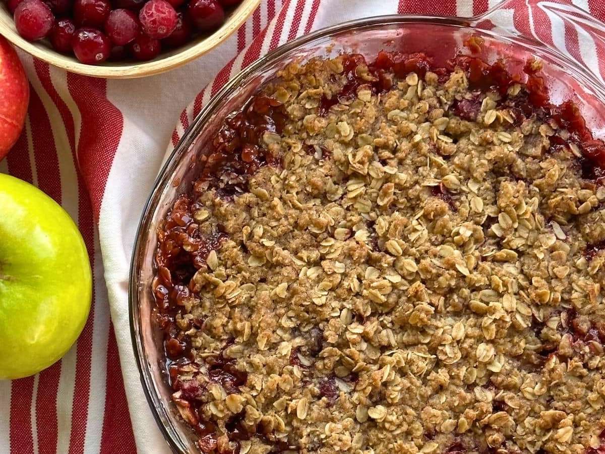 Cranberry apple crisp in pie dish next to an apple.