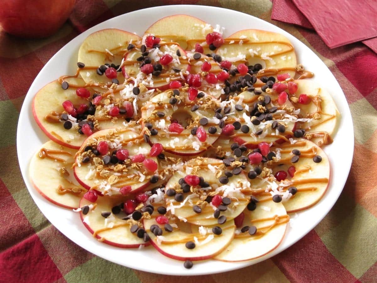 Plate of apple slices drizzled with almond butter and topped with pomegranates, chocolate chips, coconut and more to create apple nachos.