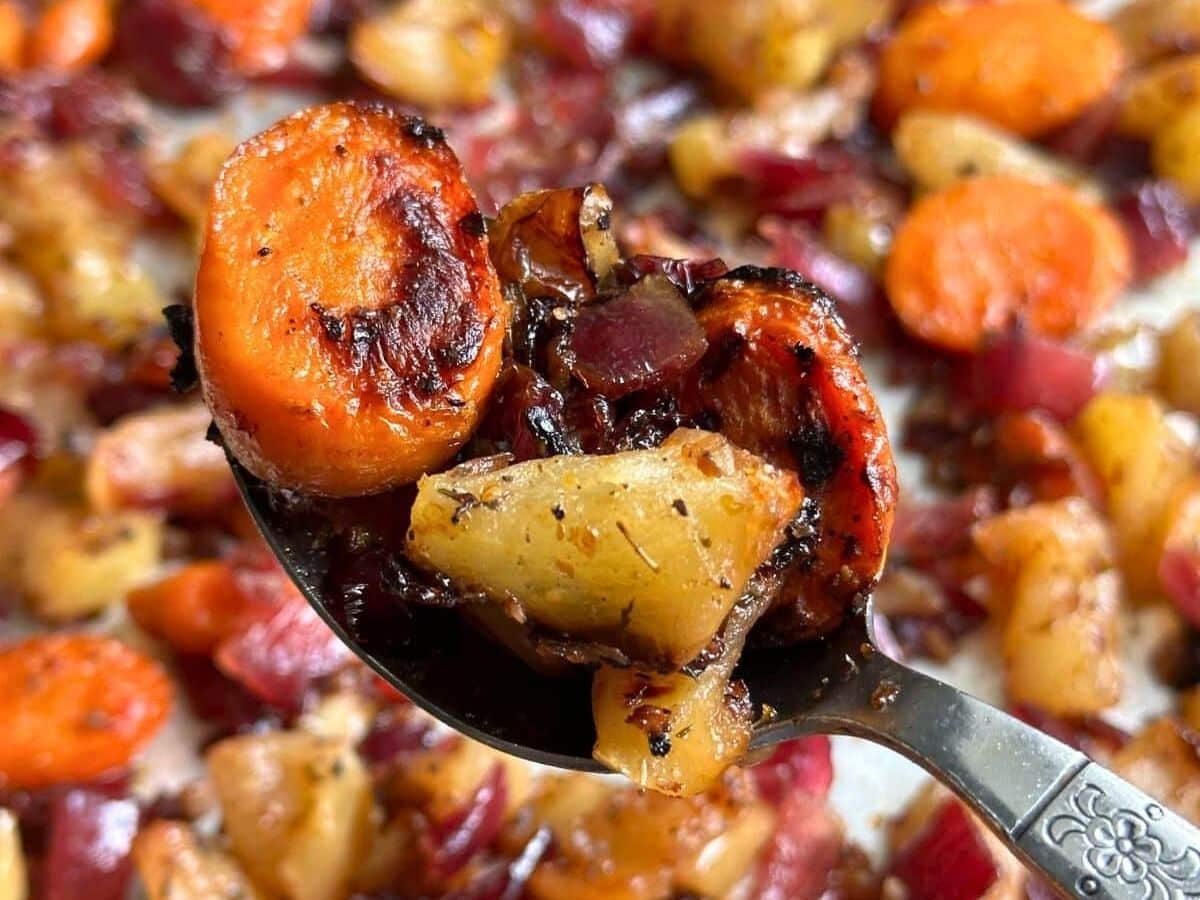 Spoon holding maple dijon roasted apples and carrots.