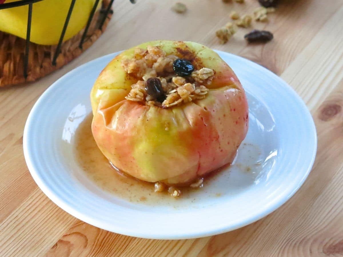 Microwave baked apple topped with granola on white plate.