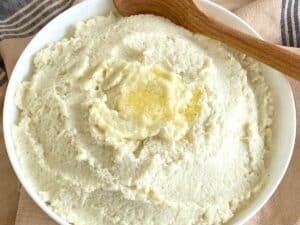 White bowl with mashed cauliflower and a wooden spoon.