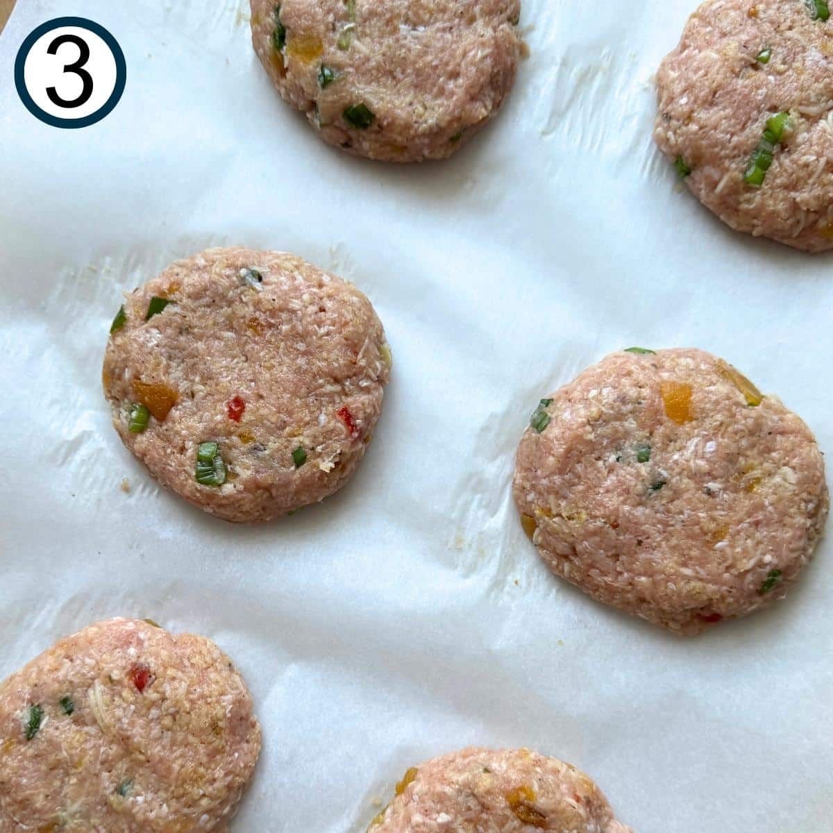 Six mango chutney turkey burger patties on parchment paper before baking in the oven.