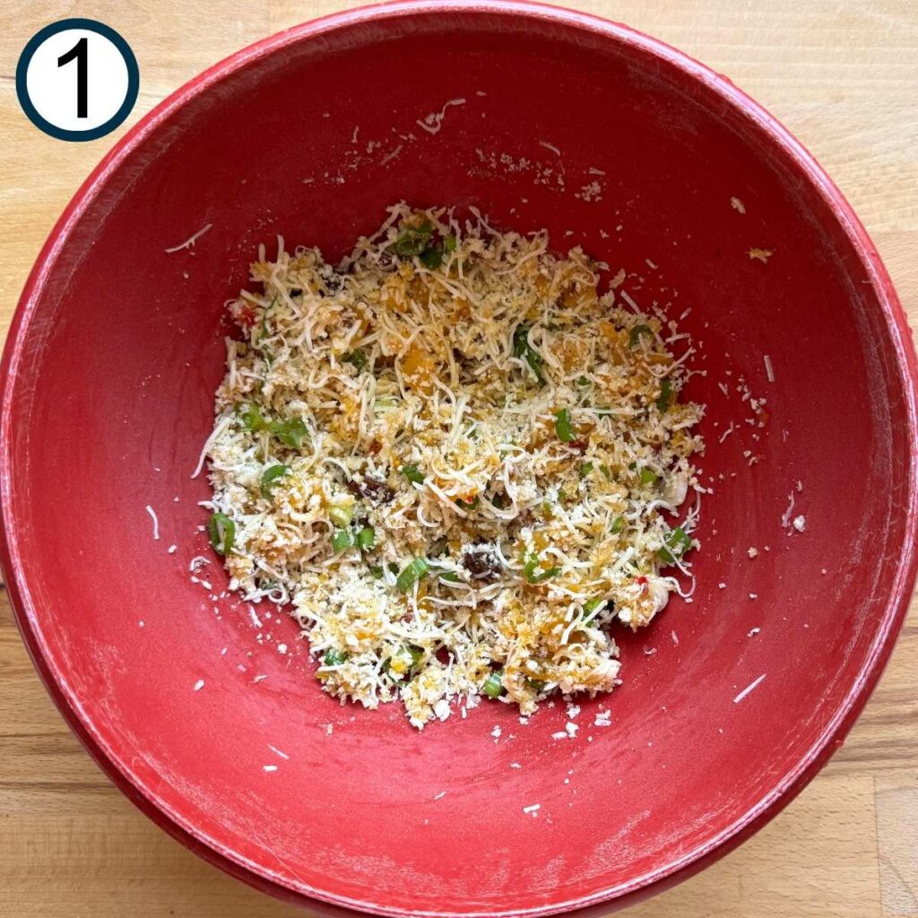 Red bowl with a mixture of panko bread crumbs, shredded mozzarella cheese, sliced green onion, mango chutney, salt, and pepper.
