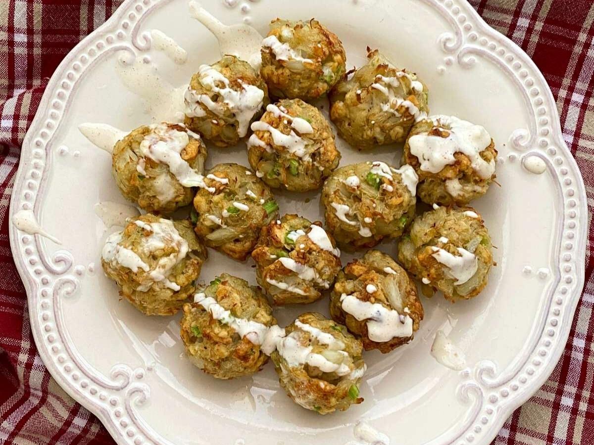 Fourteen crab balls on a white plate with aioli drizzled on top.