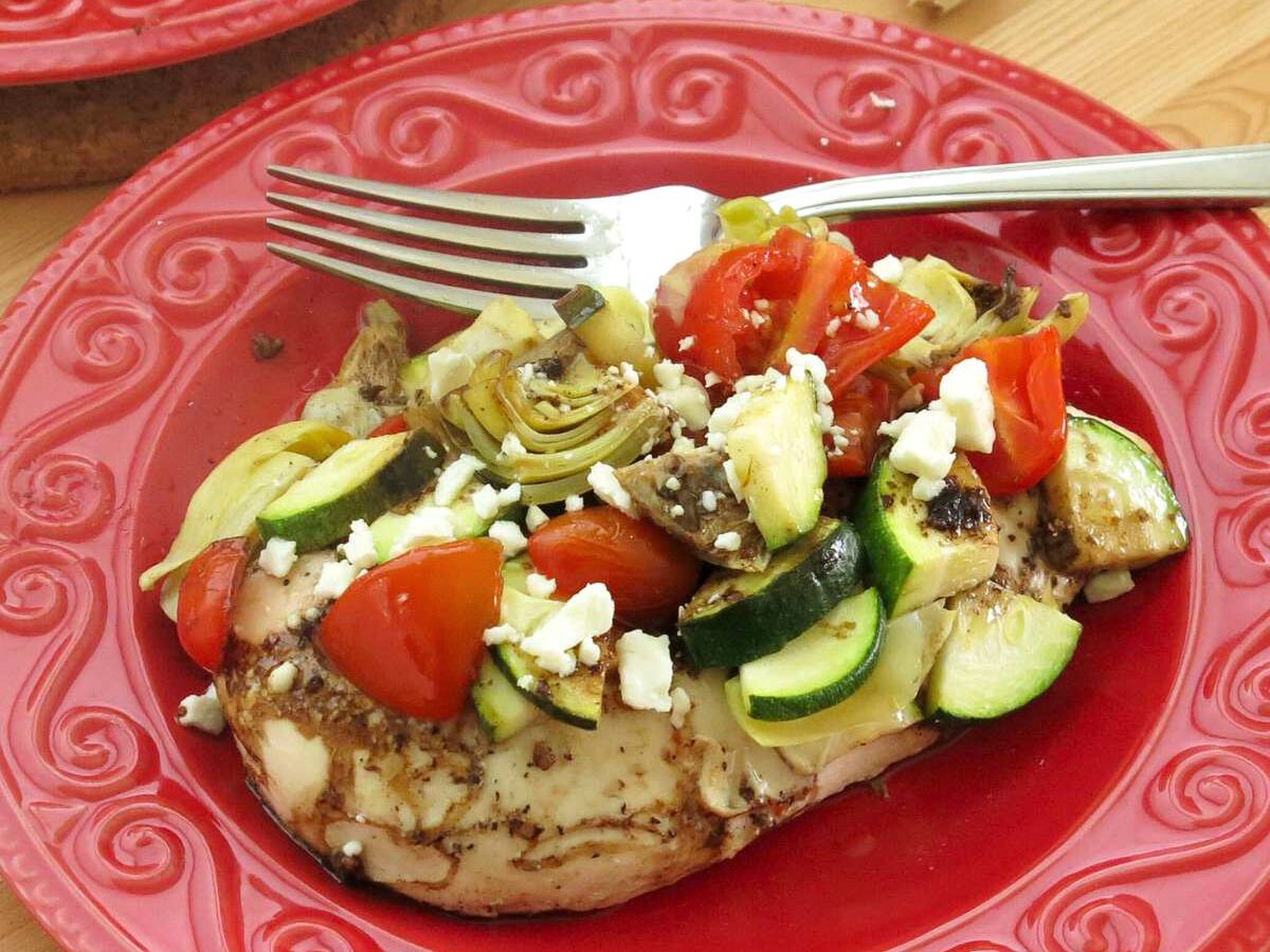 Mediterranean baked chicken with zucchini, tomatoes, and feta on a red plate.