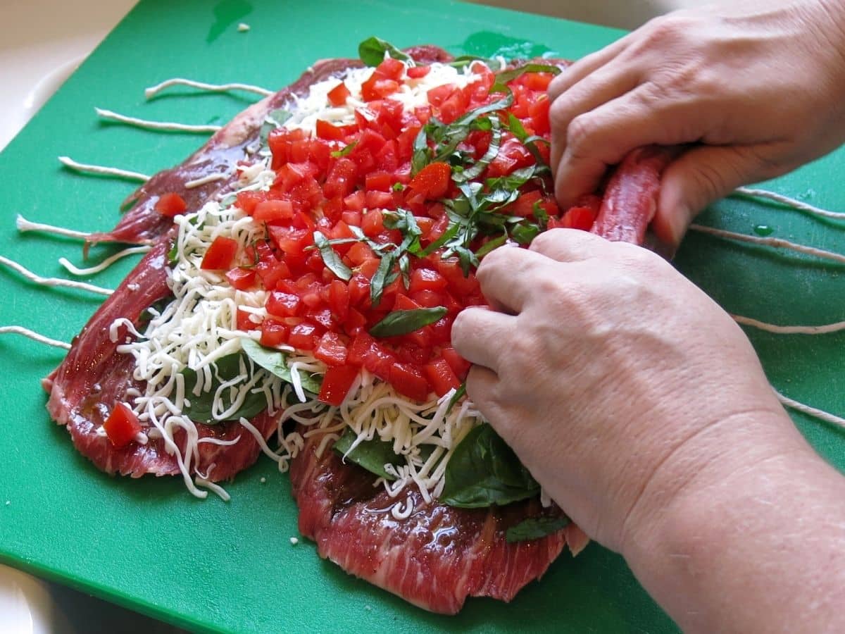 Two hands rolling a flank steak pinwheel.
