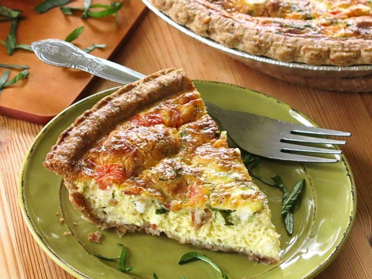 Slice of tomato bacon quiche on a green plate with a fork.