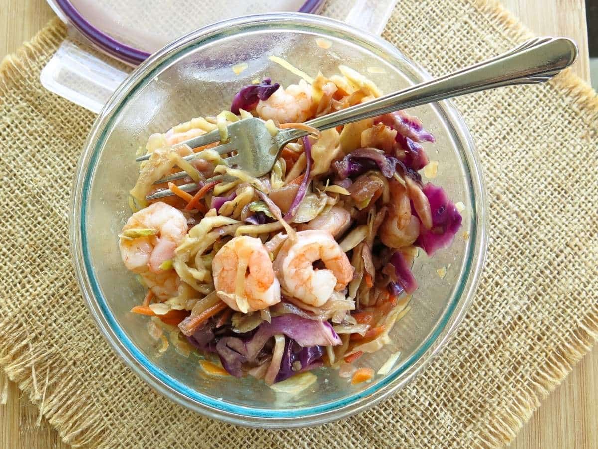 Glass container with shrimp egg roll and fork with lid behind it.