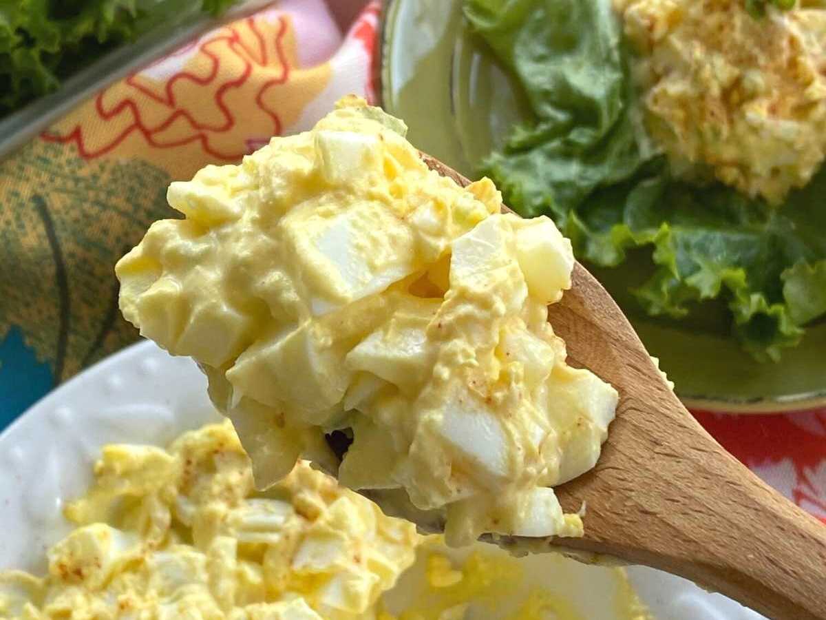 Wooden spoon lifting egg salad out of a white bowl.