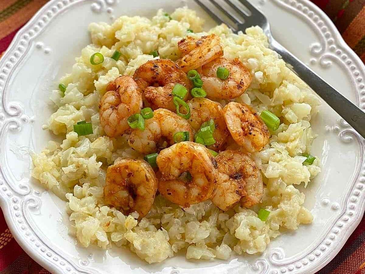Blackened shrimp on cauliflower grits with a fork on a white plate.