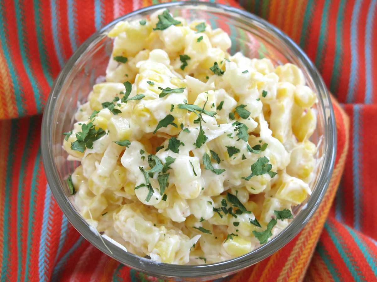 Mexican street corn salad in a glass bowl on a colorful orange napkin.