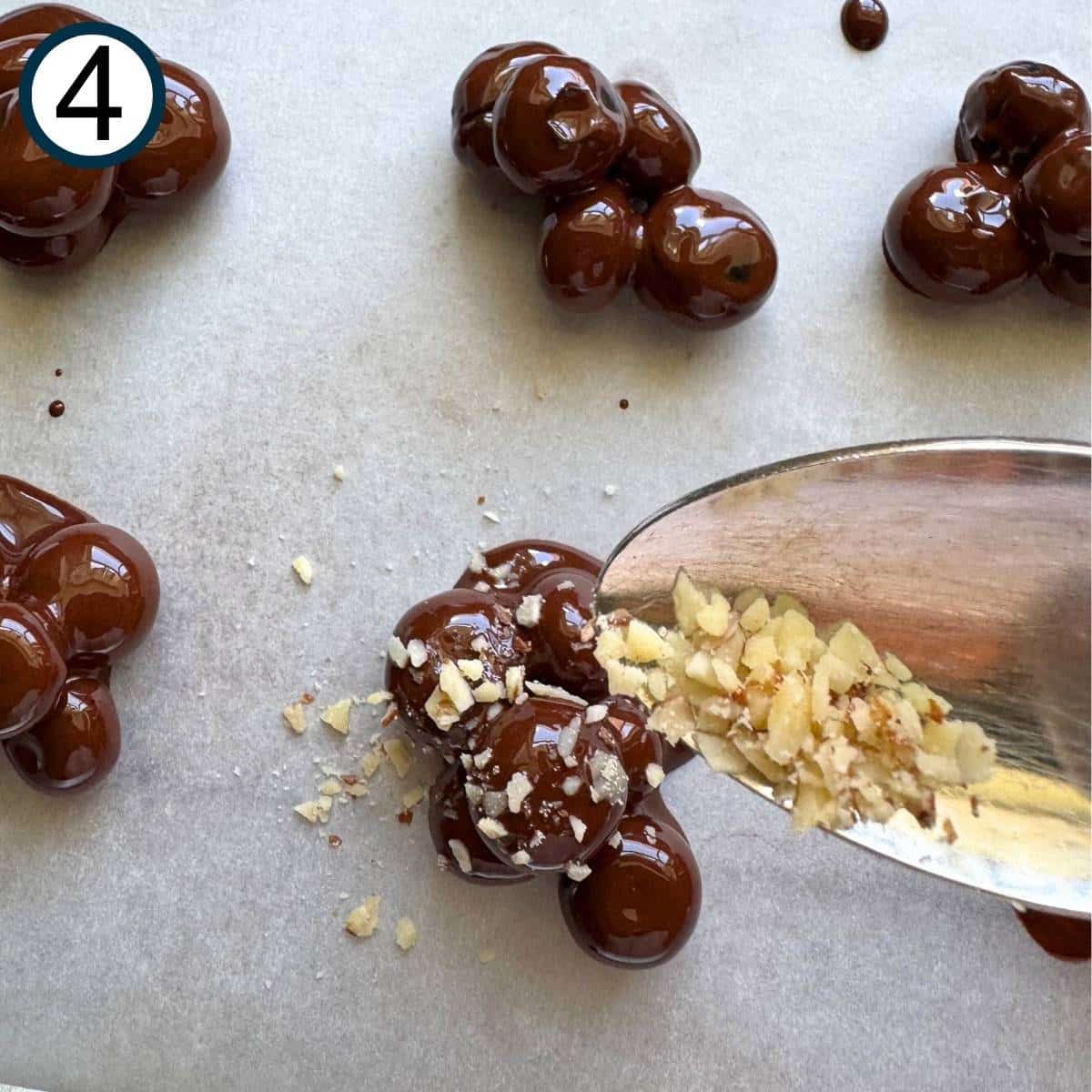 Spoon with ground almonds over a cluster of dark chocolate covered blueberries with some on top of the berries.