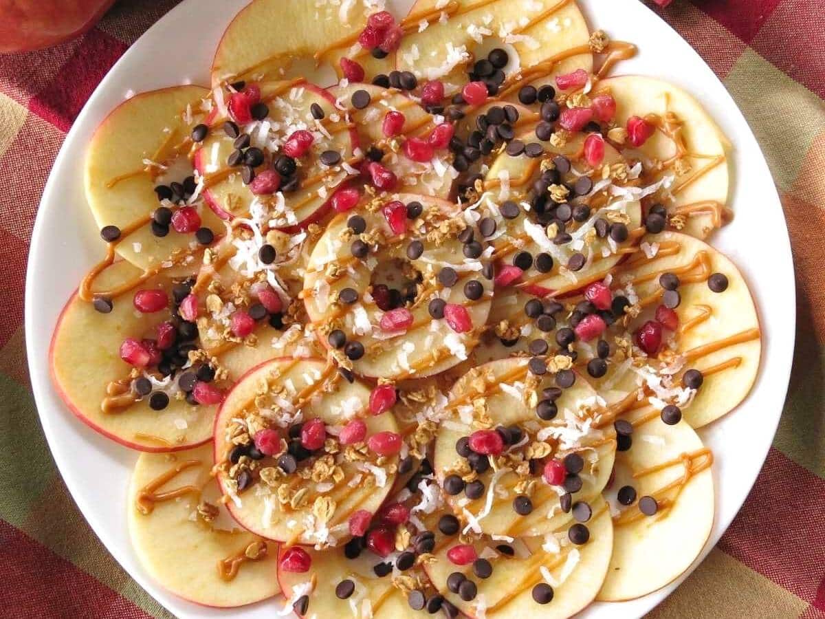 Apple dessert nachos with various toppings and almond butter drizzled over the top.