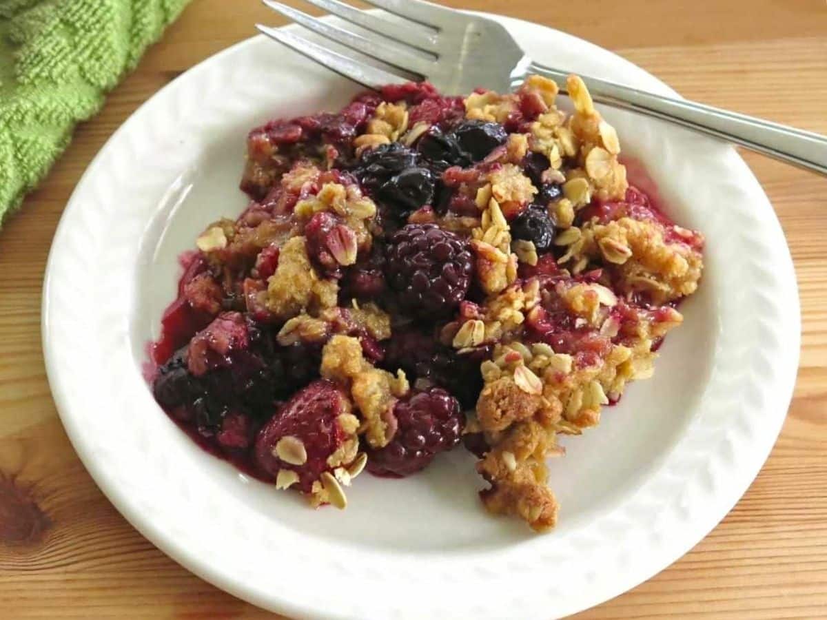 A serving of triple berry crisp on a white plate with a fork.