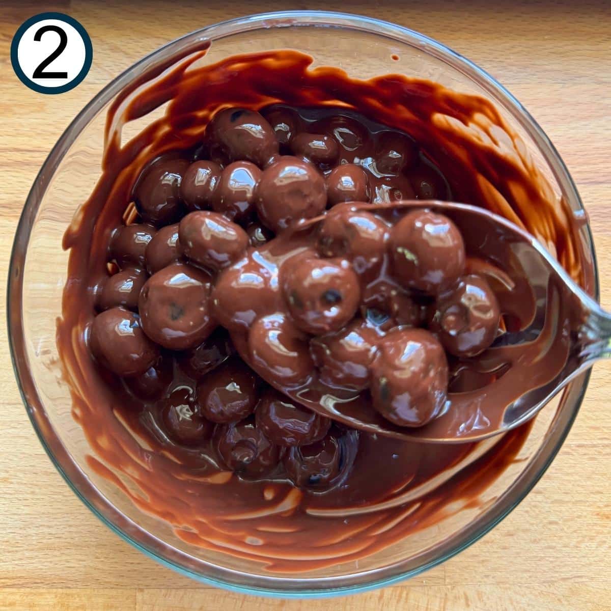 Blueberries in a glass bowl with melted chocolate and a spoon.