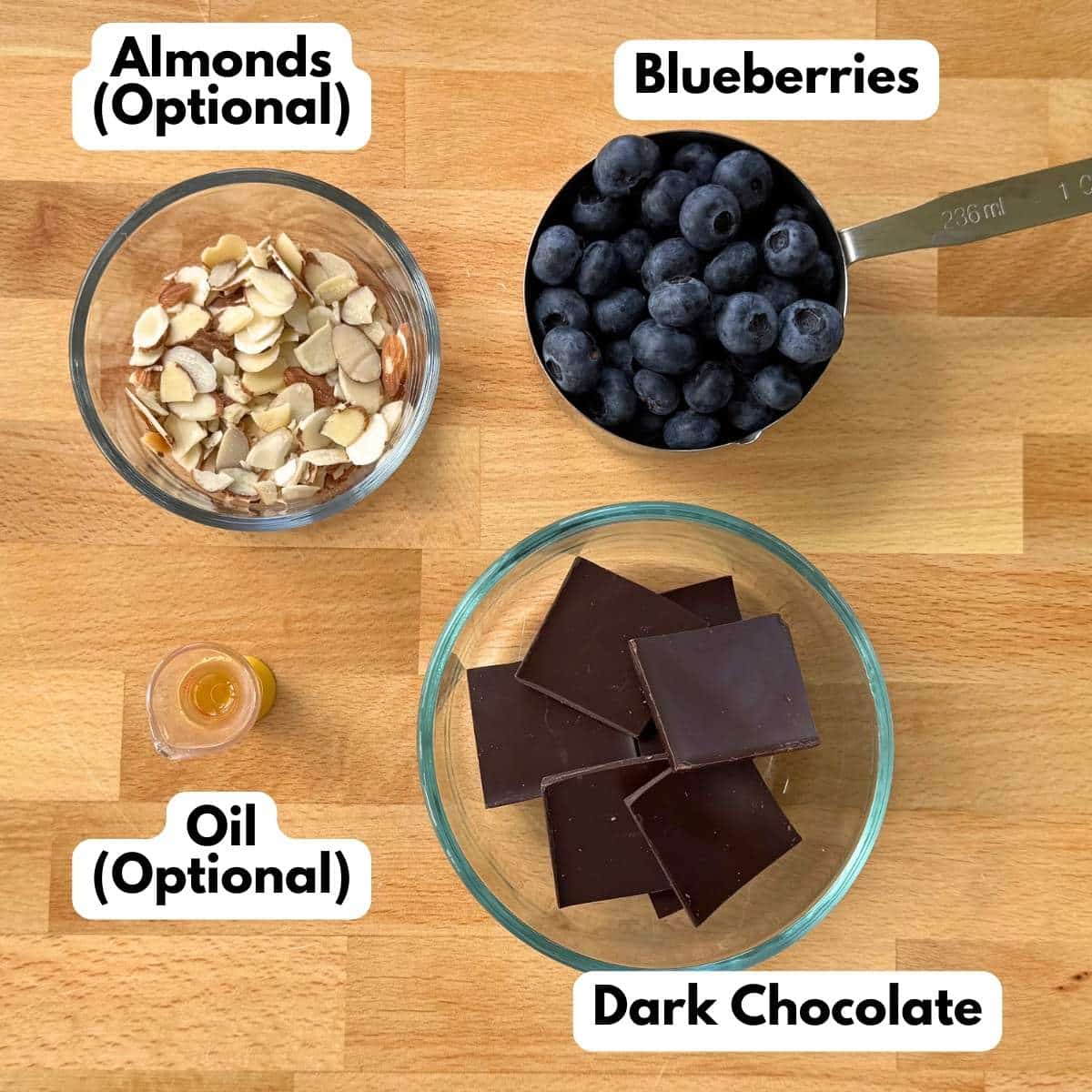 Chocolate square, blueberries, oil, and sliced almonds on a butcher block cutting board.