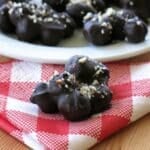 Cluster of dark chocolate covered blueberries on a red checkered napkin with more behind it.