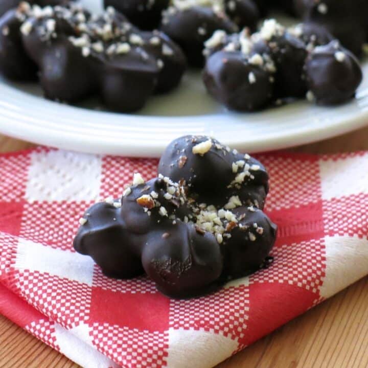 Cluster of dark chocolate covered blueberries on a red checkered napkin with more behind it.