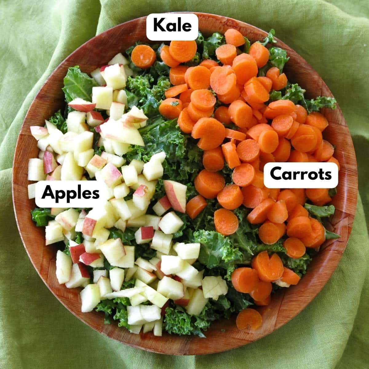 Brown bowl filled with chopped kale topped with diced carrots on one side and diced apple on the other side.