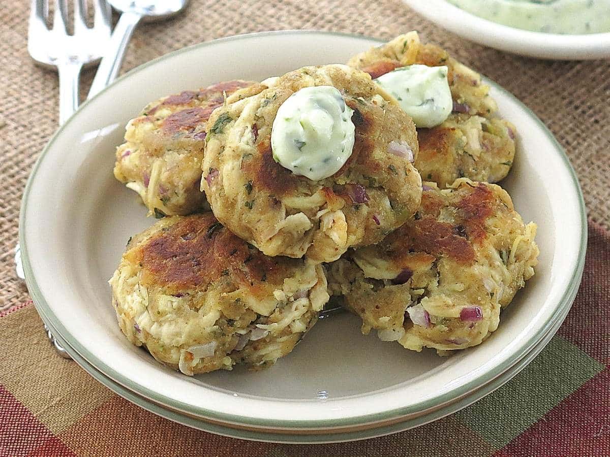 Five leftover chicken cakes on a plate with dollops of cilantro lime aioli on top.