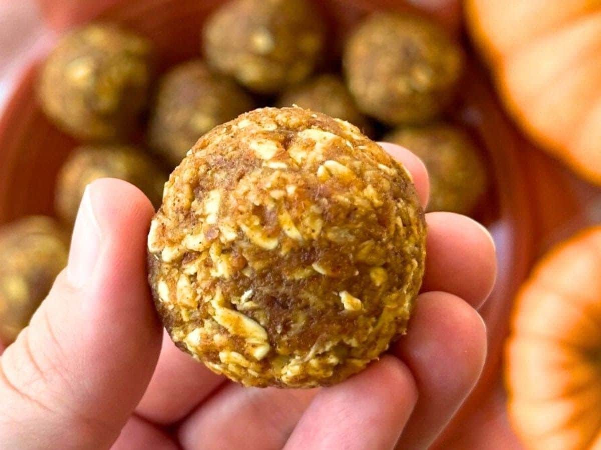 Fingers holding a pumpkin energy ball over a bowl with more of them.