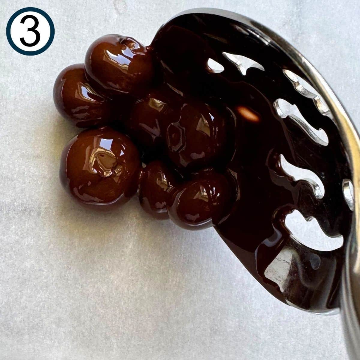 Slotted spoon lifting chocolate dipped blueberries in a cluster on parchment paper.