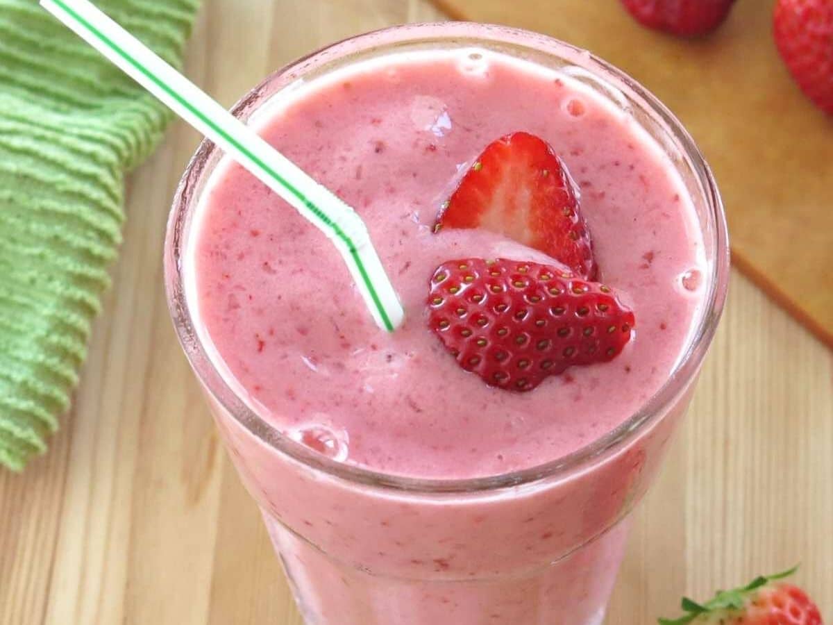 Simple strawberry smoothie with yogurt in a glass with a straw and strawberries on top.