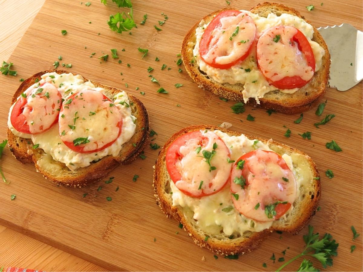 Three open-faced creamy tuna melts with cream cheese on a serving board.