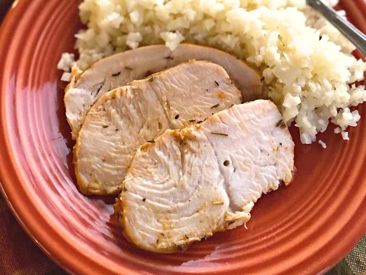 Three slices of oven-baked turkey tenderloin with cauli-rice on a rust plate.