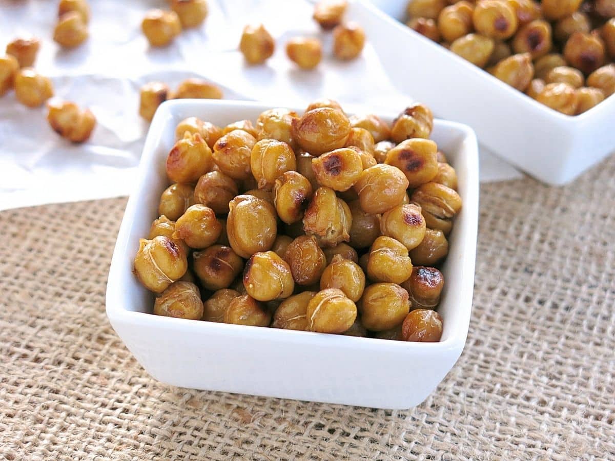Buffalo roasted chickpeas in a white container with more in the background on parchment paper.