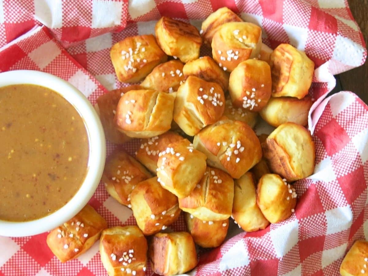 Pretzel bites next to honey mustard dipping sauce on a red checkered napkin.