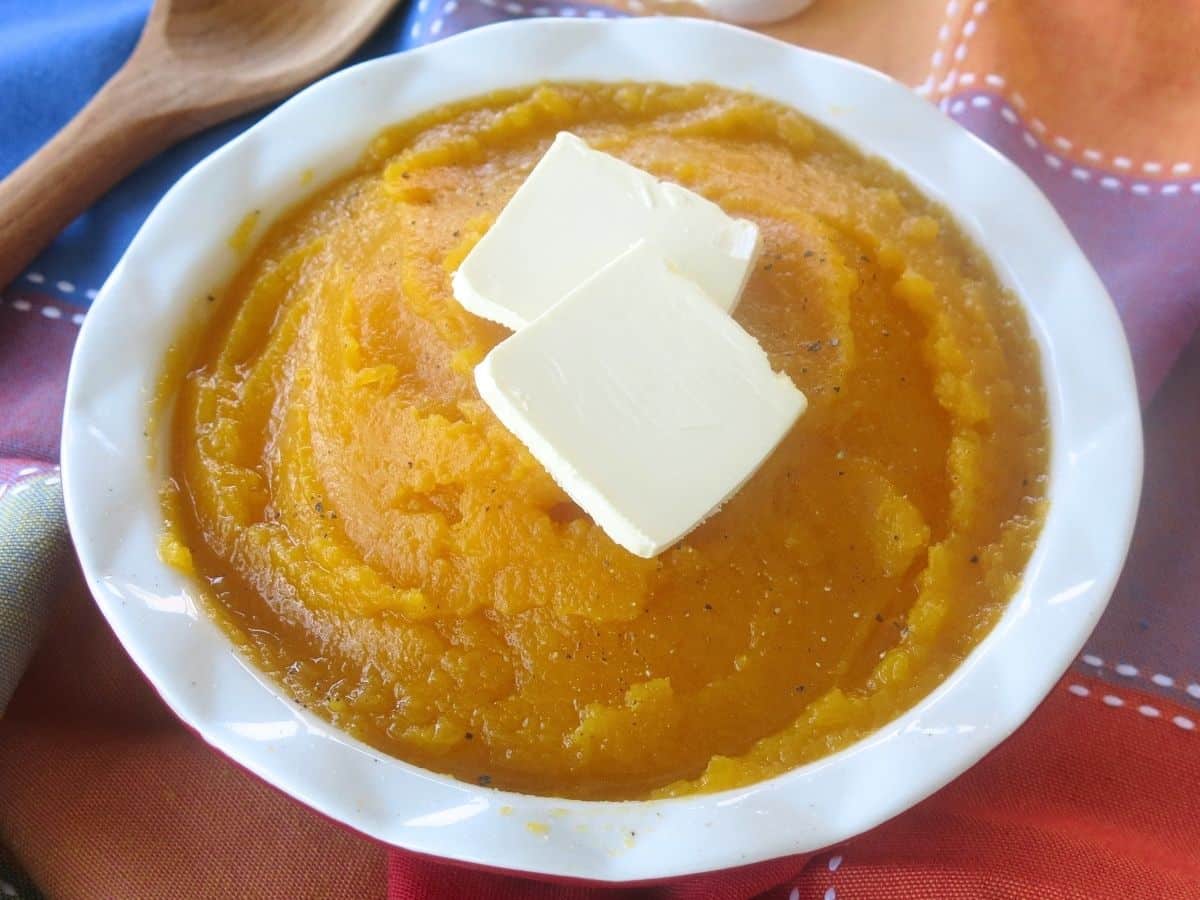 Mashed butter nut squash in a white bowl with two pats of butter on top.