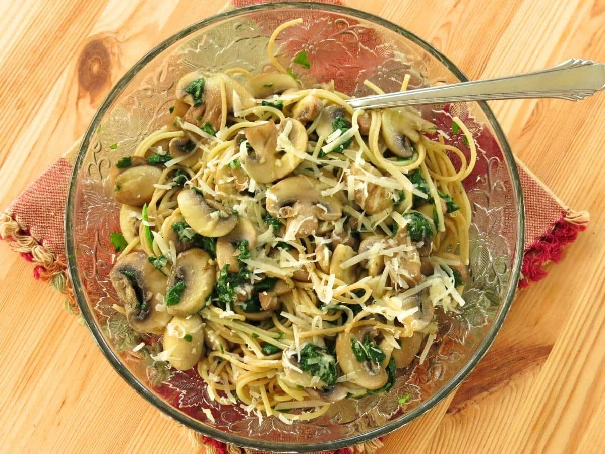 Pasta with olive oil, mushrooms, and garlic on a glass plate with a fork.