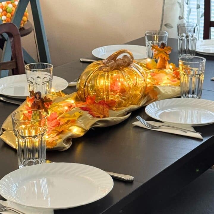 Friendsgiving tablescape with a pumpkin, fall, leaves, plates, napkins, and glasses.