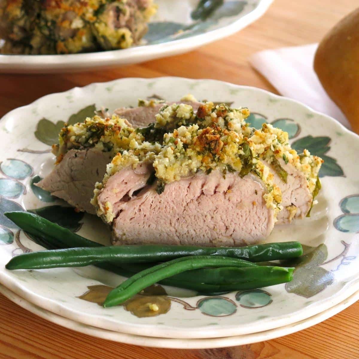 Slices of herb crusted pork tenderloin on a plate with green beans.