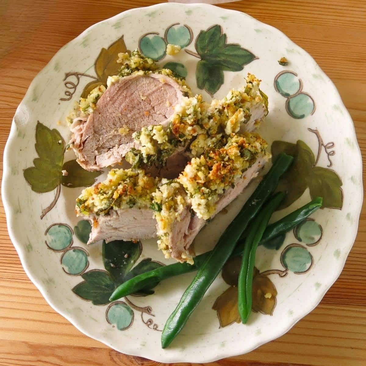 Four slices of oven backed pork tenderloin with a Parmesan herb crust on a plate with green beans.