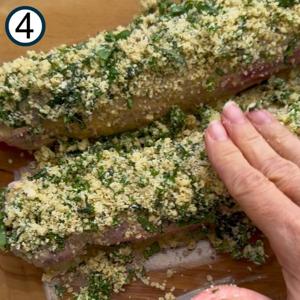 Three fingers pressing down on top of the Parmesan herb breading on a pork tenderloin.