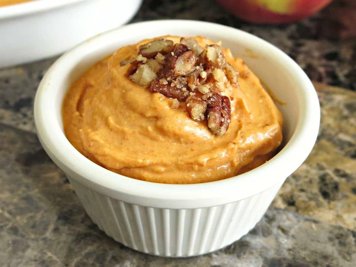 White ramekin with pumpkin cream cheese dip topped with candied pecans.