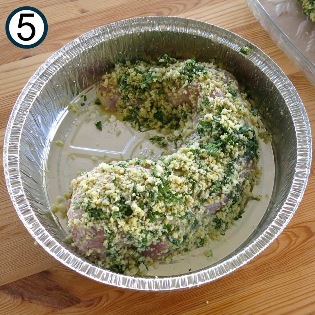 One uncooked herb crusted pork tenderloin in a round baking tin.