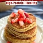 Stack of cottage cheese oat pancakes topped with diced strawberries on a white plate.