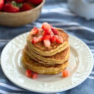 Stack of high protein cottage cheese oat pancakes topped with diced strawberries on a white plate.