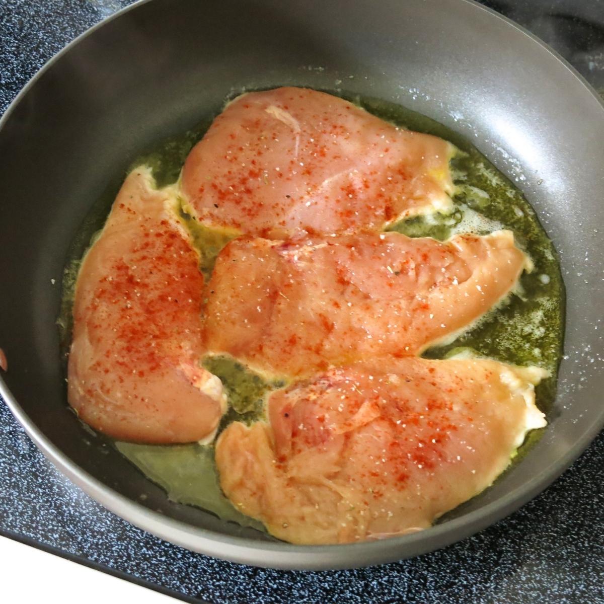 Partially cooked chicken cutlets in a skillet.