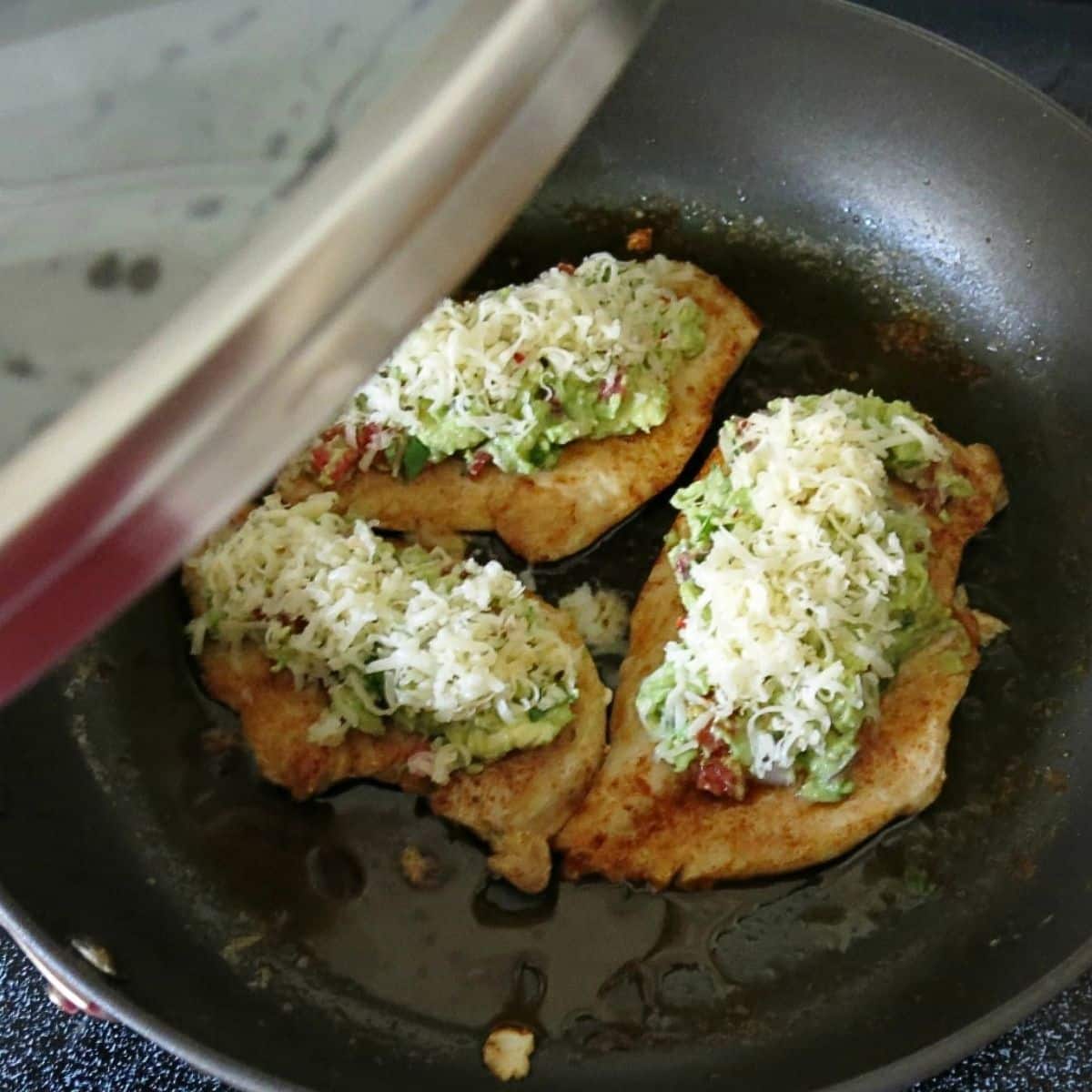 Lid starting to cover cooked chicken topped with guacamole and cheese.